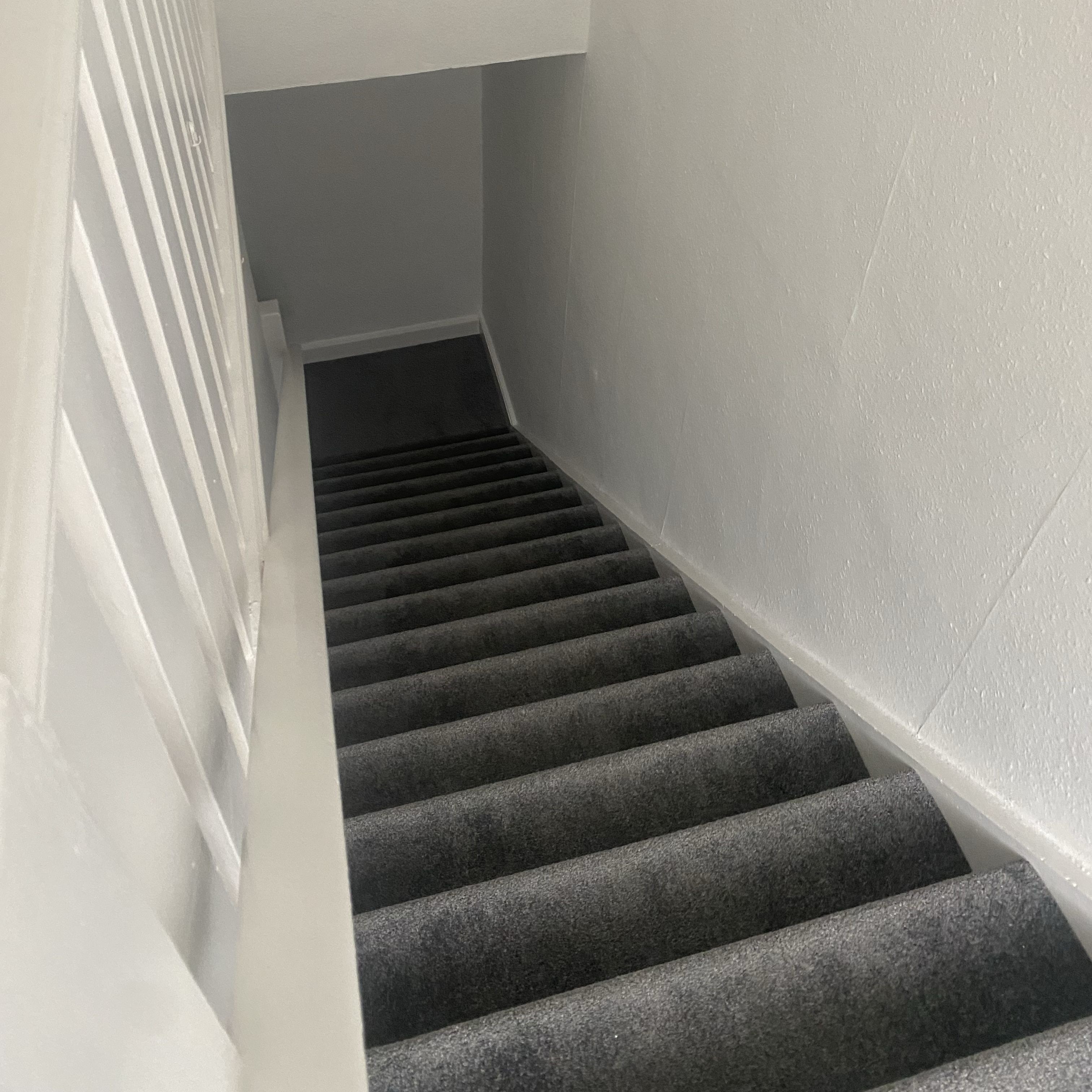 Freshly decorated staircase with new grey carpet and white painted walls and balustrade